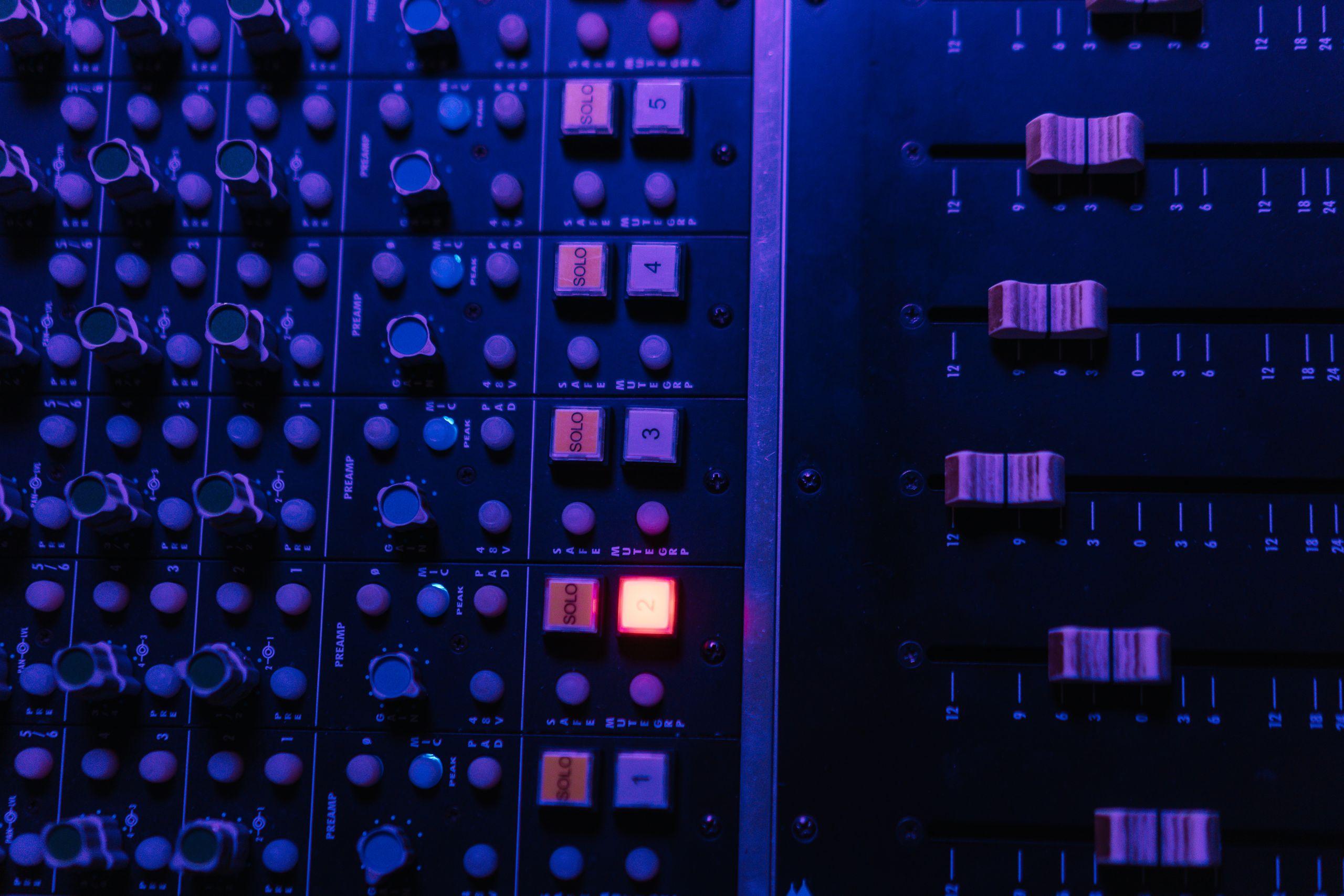Detailed view of an audio mixing console with glowing buttons and sliders under ambient lighting.